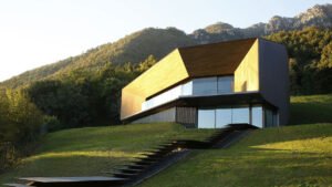 Modern Alpine Villa with angular wooden design and glass walls set on a hillside surrounded by mountains