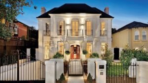 French country house style luxury home exterior with symmetrical facade, wrought iron balcony, elegant entrance gate, and warm evening lighting.