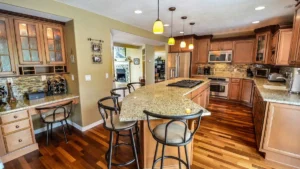 Spacious kitchen remodel featuring a large granite island, wooden cabinetry, stainless steel appliances, and hardwood flooring.
